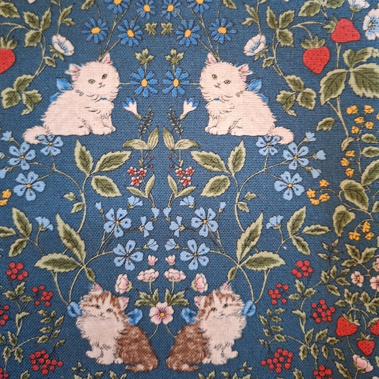 Fabric with a pattern of cats, flowers, and leaves on a blue background